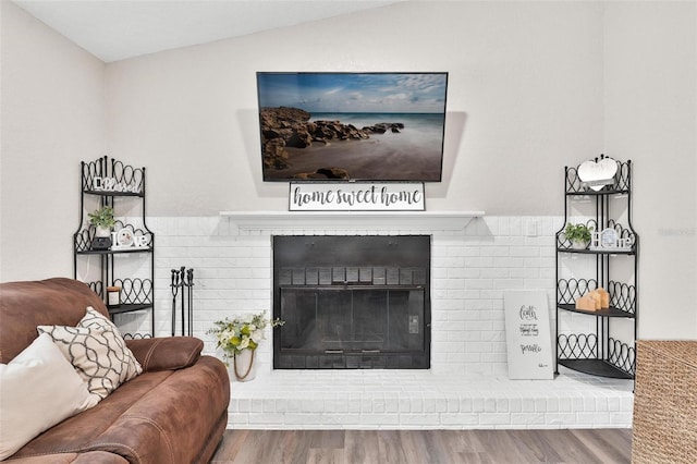 living room with vaulted ceiling, a brick fireplace, and hardwood / wood-style flooring