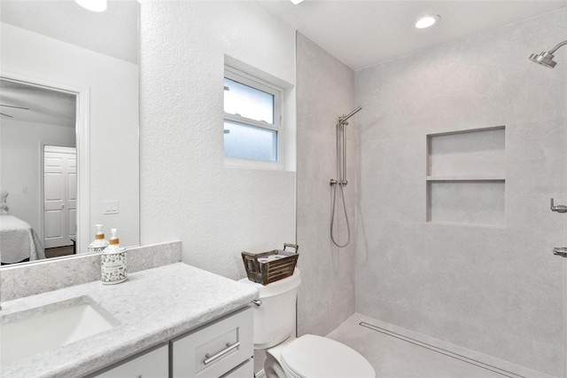 bathroom with toilet, tiled shower, and vanity