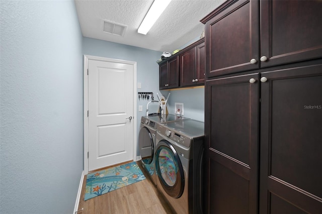 laundry area featuring light wood-type flooring, visible vents, a textured ceiling, washing machine and dryer, and cabinet space