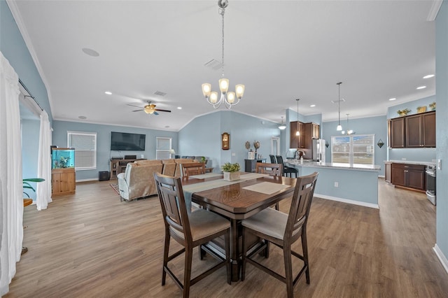 dining room with light wood finished floors, ceiling fan with notable chandelier, baseboards, and ornamental molding