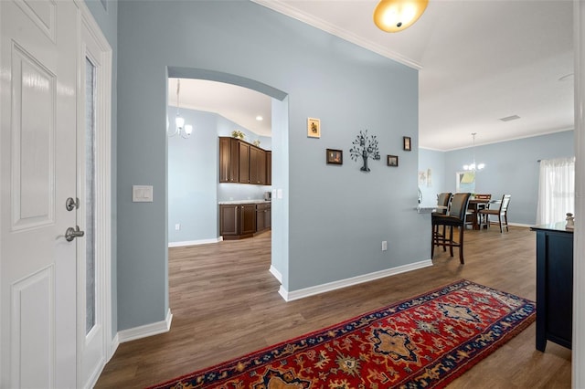 corridor with crown molding, baseboards, wood finished floors, arched walkways, and a notable chandelier