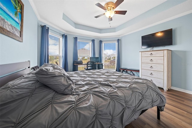 bedroom featuring a ceiling fan, wood finished floors, baseboards, a tray ceiling, and crown molding