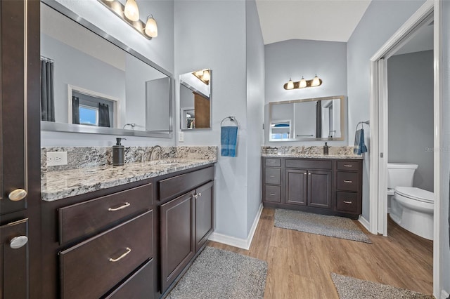 full bath featuring toilet, lofted ceiling, two vanities, wood finished floors, and a sink