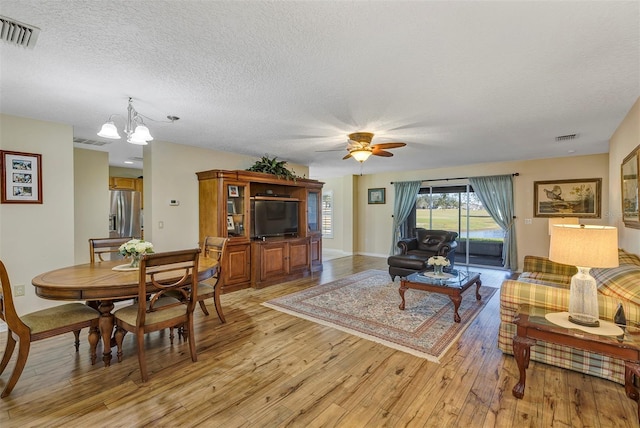 living room featuring ceiling fan with notable chandelier, a textured ceiling, and light hardwood / wood-style floors