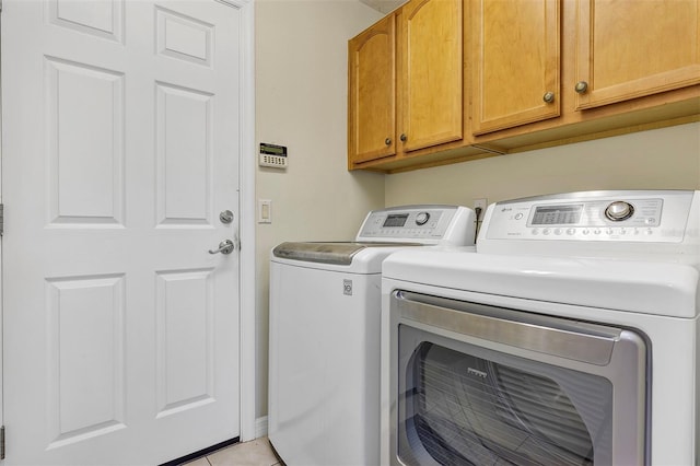 clothes washing area with cabinets, light tile patterned floors, and washing machine and clothes dryer