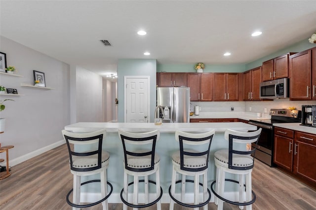 kitchen featuring tasteful backsplash, appliances with stainless steel finishes, an island with sink, and a breakfast bar area