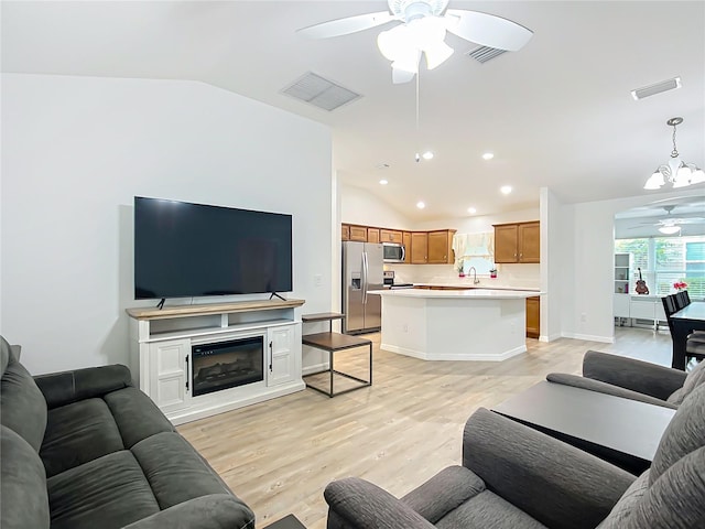 living room featuring ceiling fan with notable chandelier, sink, light wood-type flooring, and vaulted ceiling