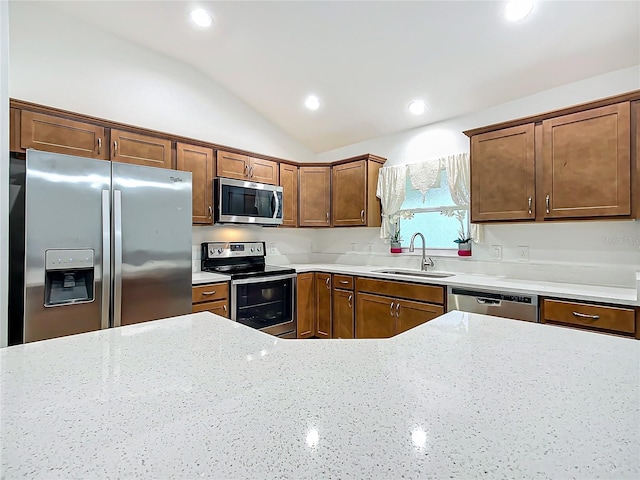 kitchen featuring vaulted ceiling, stainless steel appliances, light stone counters, and sink