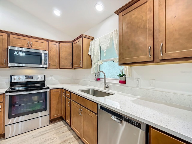 kitchen with appliances with stainless steel finishes, lofted ceiling, sink, light stone counters, and light hardwood / wood-style flooring