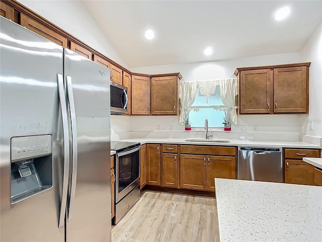 kitchen featuring light wood-type flooring, appliances with stainless steel finishes, lofted ceiling, and sink