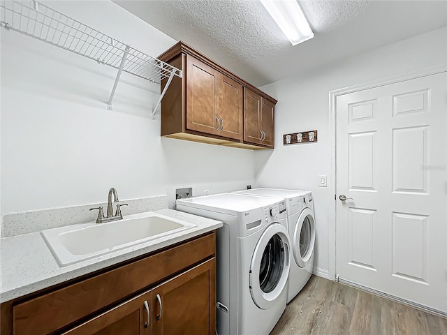 washroom with light hardwood / wood-style floors, washer and dryer, a textured ceiling, cabinets, and sink