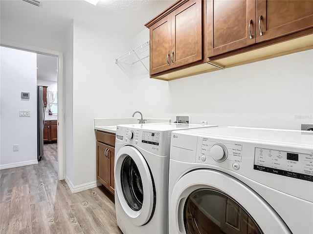 clothes washing area featuring sink, separate washer and dryer, light hardwood / wood-style floors, and cabinets