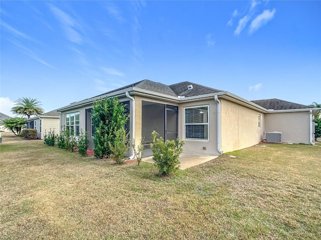 rear view of property featuring central AC unit, a lawn, and a sunroom