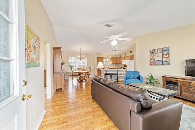 living room with lofted ceiling, ceiling fan with notable chandelier, a textured ceiling, and light wood-type flooring