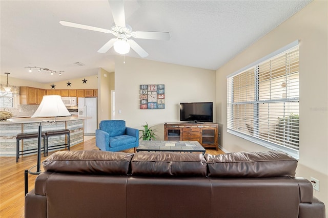 living room with vaulted ceiling, ceiling fan, a textured ceiling, and light wood-type flooring