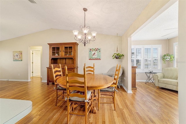 dining area featuring lofted ceiling, a chandelier, a textured ceiling, and light wood-type flooring