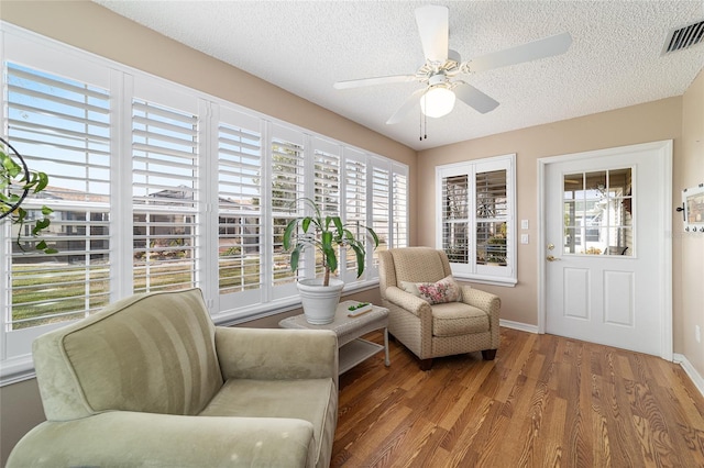 living area featuring wood-type flooring, a wealth of natural light, a textured ceiling, and ceiling fan