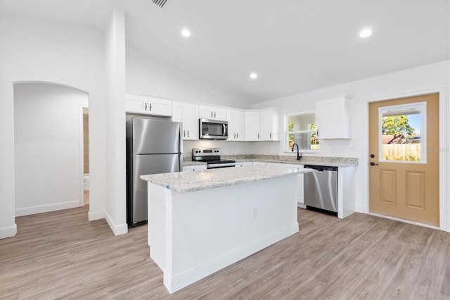 kitchen with appliances with stainless steel finishes, light wood-type flooring, a kitchen island, white cabinets, and sink