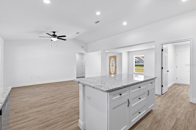 kitchen with lofted ceiling, light hardwood / wood-style floors, a kitchen island, white cabinets, and light stone counters