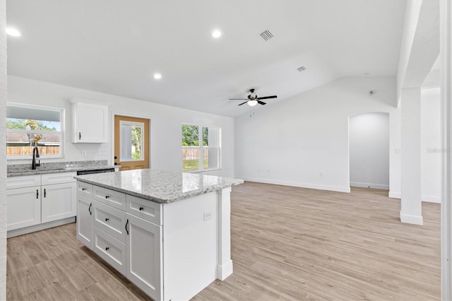 kitchen with light stone countertops, a kitchen island, white cabinetry, vaulted ceiling, and light hardwood / wood-style flooring