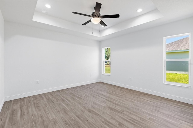 empty room featuring light hardwood / wood-style floors, a tray ceiling, and ceiling fan