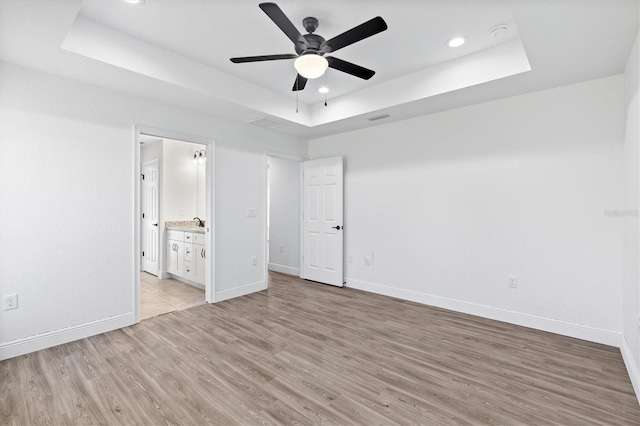 unfurnished bedroom featuring ceiling fan, light hardwood / wood-style floors, a raised ceiling, and ensuite bath