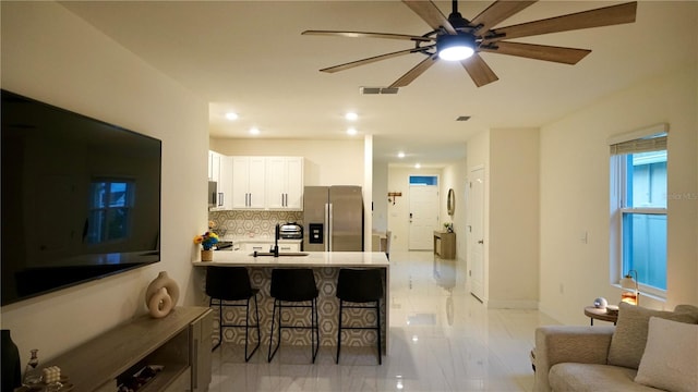 kitchen with white cabinetry, kitchen peninsula, stainless steel fridge, a breakfast bar area, and tasteful backsplash