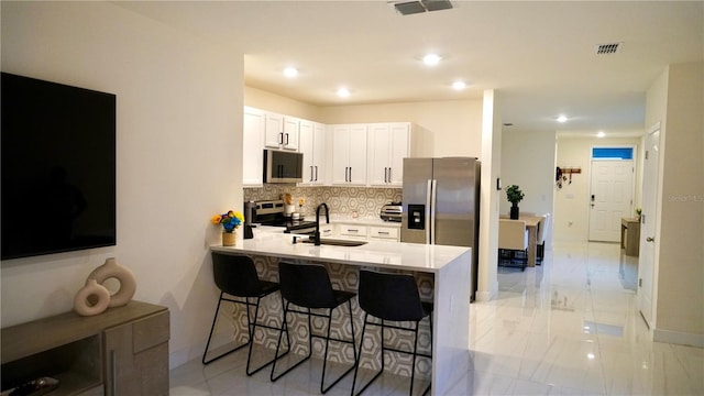 kitchen with backsplash, a breakfast bar, kitchen peninsula, stainless steel appliances, and white cabinets