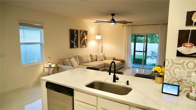 kitchen featuring ceiling fan, stainless steel dishwasher, white cabinets, light stone counters, and sink