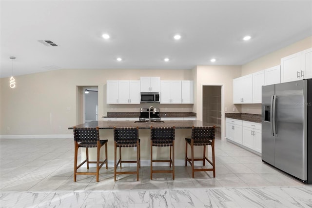 kitchen with stainless steel appliances, a center island with sink, white cabinets, and a kitchen breakfast bar