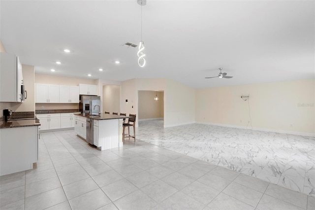 kitchen with hanging light fixtures, appliances with stainless steel finishes, an island with sink, ceiling fan, and white cabinets