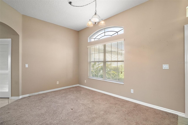 empty room featuring light colored carpet, a textured ceiling, and a chandelier