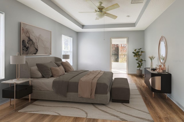 bedroom with access to outside, hardwood / wood-style flooring, ceiling fan, and a raised ceiling