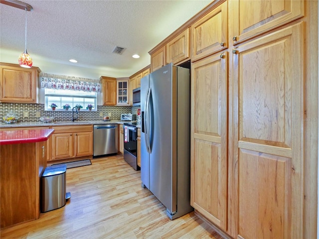 kitchen with sink, appliances with stainless steel finishes, tasteful backsplash, light hardwood / wood-style floors, and a textured ceiling