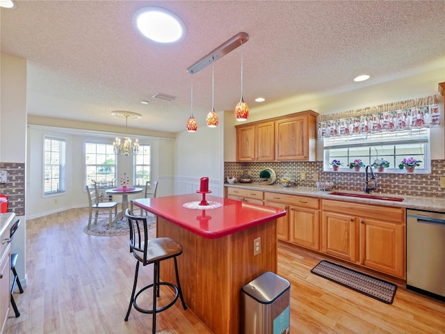 kitchen with decorative light fixtures, dishwasher, sink, a center island, and light wood-type flooring