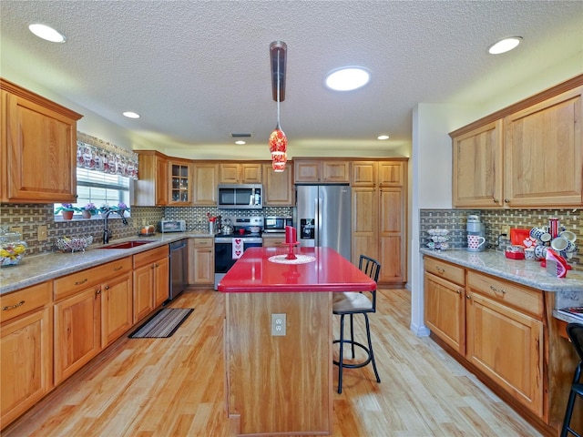 kitchen featuring a breakfast bar area, decorative light fixtures, light hardwood / wood-style flooring, a kitchen island, and stainless steel appliances