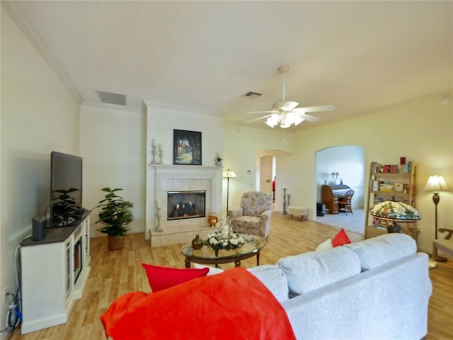 living room featuring ornamental molding, a tile fireplace, ceiling fan, and light wood-type flooring