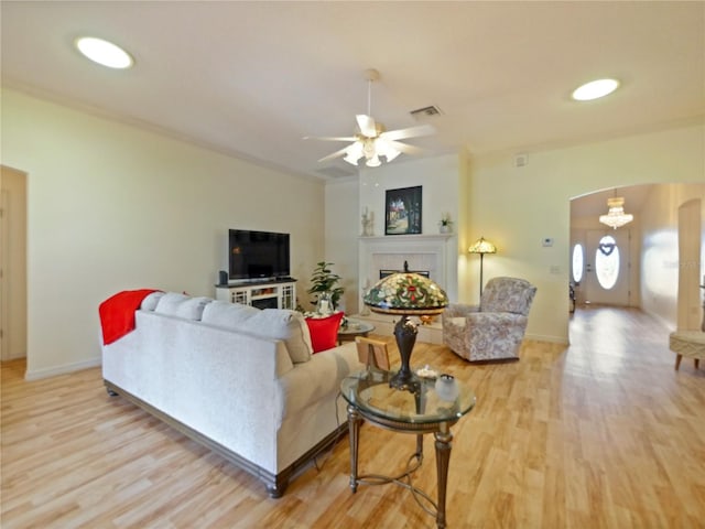 living room featuring a fireplace, ceiling fan, and light wood-type flooring