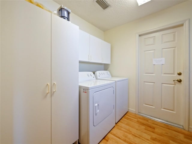 laundry room featuring cabinets, a textured ceiling, washing machine and clothes dryer, and light wood-type flooring