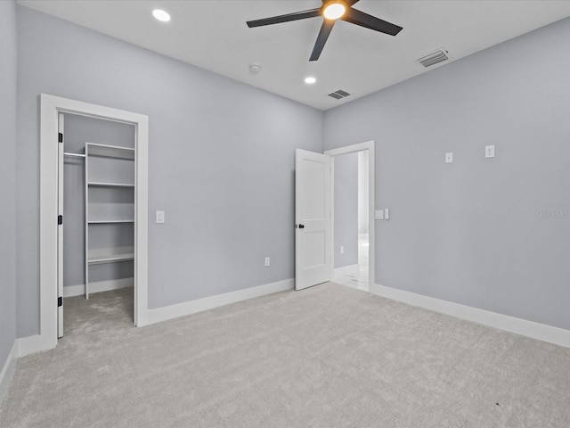 unfurnished bedroom featuring a spacious closet, a closet, light carpet, and ceiling fan