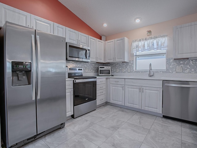 kitchen with lofted ceiling, white cabinetry, stainless steel appliances, sink, and backsplash