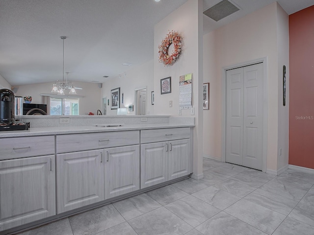 kitchen featuring white cabinetry, pendant lighting, lofted ceiling, and a notable chandelier