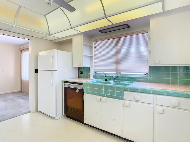 kitchen with sink, tile countertops, dishwasher, white fridge, and white cabinets