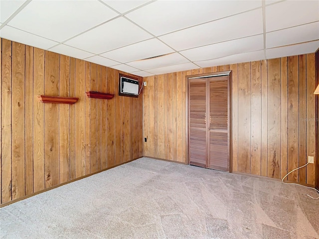 unfurnished bedroom with a paneled ceiling, light carpet, and wood walls