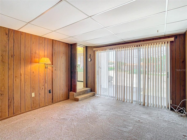 unfurnished room with a drop ceiling, wooden walls, and carpet flooring