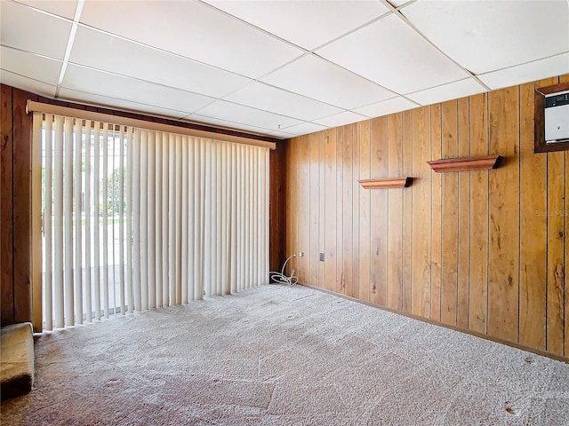 unfurnished room with a drop ceiling, carpet floors, and wood walls