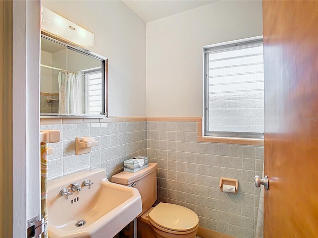 bathroom with a shower with shower curtain, toilet, sink, and tile walls