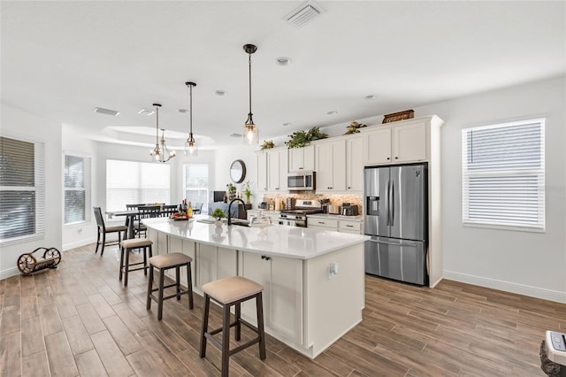 5857 Mackenzie Ave, The Villages, FL 32163 - kitchen with visible vents, a breakfast bar, a kitchen island with sink, stainless steel appliances, and backsplash