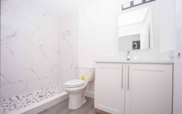 bathroom with hardwood / wood-style flooring, a tile shower, vanity, and toilet