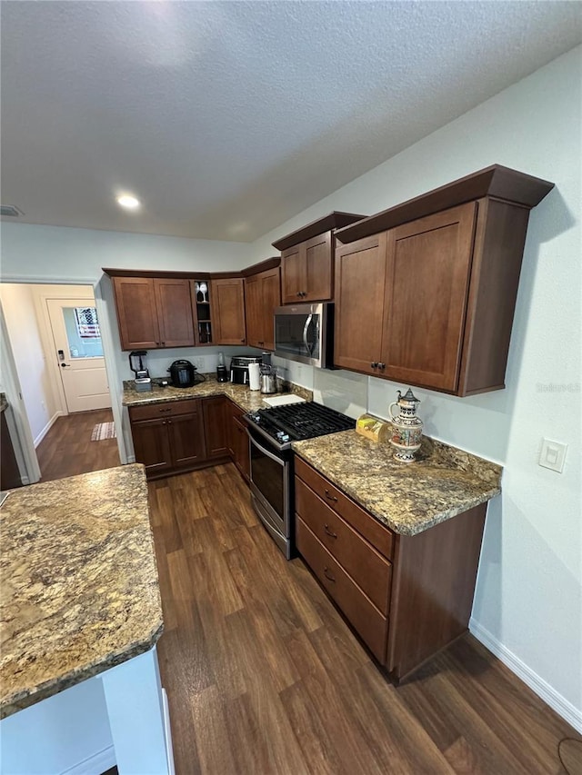 kitchen with dark brown cabinetry, stone countertops, a textured ceiling, dark hardwood / wood-style floors, and stainless steel appliances